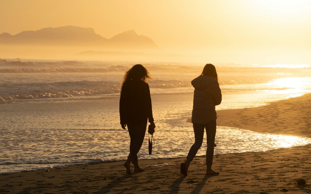 two women walking on the beach at sunset